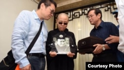 刘晓波遗孀刘霞手捧遗像。刘晓波弟弟刘晓瑄（右）和刘霞弟弟刘晖陪伴（沈阳市政府公布图片）