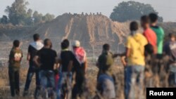 2015年10月以色列和加沙地带边界附近的冲突期间，巴勒斯坦抗议者注视掩护在沙丘后面的以军士兵。