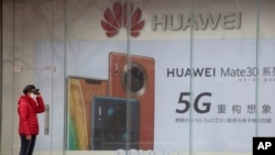 北京，一位戴着口罩的妇女站在华为手机广告旁（2020年3月8日）。