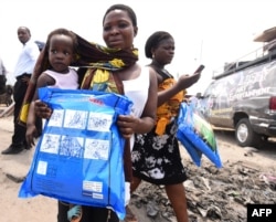 FILE - A woman carrying a baby holds a treated mosquito net during a malaria prevention action at Ajah in Eti Osa East district of Lagos, Nigeria, April 21, 2016.