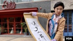 香港記者協會主席鄭嘉如展示其中一項網上籌款拍賣品，香港填詞人潘源良 "邁步向前" 書法墨寶。(美國之音)