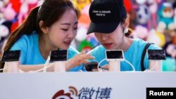  2018年4月27日，在北京舉行的全國移動互聯網大會（GMIC）期間，工作人員在新浪微博的攤位上使用智能手機。一個人的帽上有英文，意思是“我是來讓人心碎的”。 