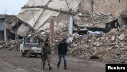 反政府武裝戰士在位於阿勒頗鄉村的阿拉伊鎮被毀壞的建築物旁行走(2016年12月30日)