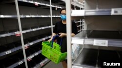 一名戴口罩的新加坡妇女星期六（2月8日）在商店购物。货架上的方便面和罐头食品似乎已被抢购一空。 