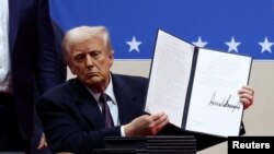 Трамп показывает подписанный им документ на сцене стадиона Capital One Arena