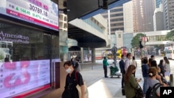 2021年2月22日人们走过显示香港股票指数的银行电子板。