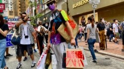 香港异见艺术家黄国才2020年7月1日，香港国安法实施第一日，在铜锣湾以”血拼”为名，打扮成来自中国大陆的”豪客”，手持多个写上国安法相关罪名的百货公司购物袋，表现对实施国安法的不安 （美国之音/汤惠芸）