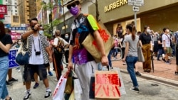 香港異見藝術家黃國才2020年7月1日，香港國安法實施第一日，在銅鑼灣以”血拼”為名，打扮成來自中國大陸的”豪客”，手持多個寫上國安法相關罪名的百貨公司購物袋，表現對實施國安法的不安 （美國之音/湯惠芸）