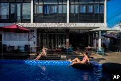 ນັກທ່ອງທ່ຽວຊາວຕ່າງປະເທດກຳລັງພັກຜ່ອນຢ່ອນອາລົມຢູ່ທີ່ສະລອຍນ້ຳຂອງບ້ານພັກ Nana Backpacker Hostel ໃນເມືອງວັງວຽງ, ສປປ ລາວ, ເມື່ອວັນອັງຄານ ທີ 19, 2024. (AP Photo/Anupam Nath)