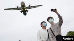 兩名戴著口罩的青年正在以即將降落在台灣台北松山機場的飛機做背景自拍。（2020年3月29日）