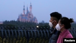 戴着口罩的上海市民从春节期间关闭的迪斯尼乐园旁走过。（2020年1月24日）