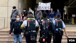 2024年11月19日，香港民主派初选案被告吕智恒的养母Elsa在吕智恒被判刑后，在西九龙裁判法院大楼外高举”义人得生、恶人必亡”的标语。她立即被多名香港警员包围及带上警车。 (美国之音照片) 