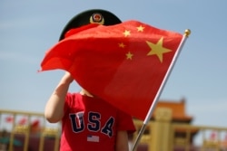 一名站在北京天安门广场的小男孩身穿美国T恤手拿中国国旗。（2019年5月7日）