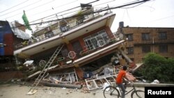 4月28日加德滿都一名男孩騎車經過因地震後倒塌的樓房前。