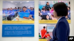 在烏魯木齊舉辦的打擊恐怖主義與極端主義的展覽會上，一名解說員站在顯示新疆維吾爾等少數民族在訓練營裡的生活照片前。（2021年4月21日）