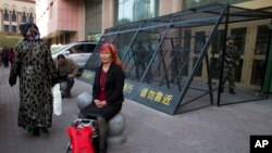 2014年5月1日，一名維吾爾族婦女在一個由中國武警重兵把守的大樓入口處休息。