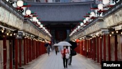 东京市民戴着口罩走在关闭的商店旁。（2021年5月7日）