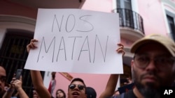 A man holds a sign that reads in Spanish "They are killing us" while demanding the resignation of Governor Wanda Vazquez after the discovery of an old warehouse filled with unused emergency supplies in San Juan, Puerto Rico, Jan. 20, 2020.