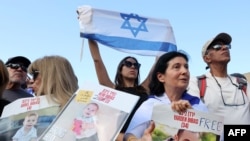 2025 年2 月1 日，大衆在特拉維夫人質廣場的屏幕上觀看釋放加沙地帶的以色列人質時，他們舉著剛獲釋的以色列人質亞登·比巴斯(Yarden Bibas) 及其兩個孩子科菲爾(Kfir) 和阿里爾(Ariel) 的照片。