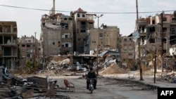 一名男子2月10日骑摩托车经过残破不堪的哈拉斯塔市（Harasta）。这座城市位于叙利亚首都大马士革以东。
