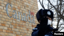 在加拿大驻北京大使馆外一名中国警察向摄影记者打禁止的手势。（2018年12月12日）