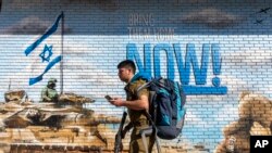 Израильский военный проходит мимо граффити с призывом вернуть заложников, похищенных во время нападения ХАМАС на Израиль 7 октября 2023 года. (AP Photo/Ariel Schalit)