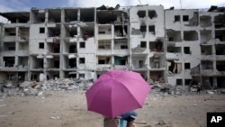 一名巴勒斯坦男孩打着伞在加沙地带北部的一处遭到破坏的居民区休息（2014年8月11日）