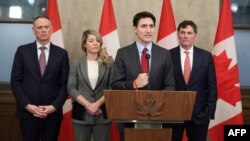 ນາຍົກລັດຖະມົນຕີການາດາ ທ່ານ ຈັສຕິນ ທຣູໂດ ກ່າວປາສ, ເຊິ່ງຢືນຄຽງຂ້າງໂດຍ (ຈາກຊ່າຍຫາຂວາ), ລັດຖະມົນຕີດ້ານຄວາມປອດໄພທາງສັງຄົມ ທ່ານ ເດວິດ ແມັກຄວິນຕີ, ລັດຖະມົນຕີກະຊວງການຕ່າງປະເທດ ທ່ານນາງ ເມີລານີ ໂຈລີ, ພ້ອມດ້ວຍລັດຖະມົນຕີກະຊວງການເງິນ ແລະກິດຈະການພາຍໃນຂອງລັດຖະບານ ທ່ານ ໂດມີນິກ ເລີບລັງ.