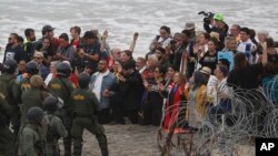 2018年12月10日，在墨西哥蒂華納的隔離牆附近看到，在圣迭戈，美國警方和邊境巡邏隊面對一個支持中美洲尋求庇護者的跨信仰團體的成員。