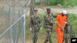 ນັກໂທດທີ່ຕິດຄຸກຢູ່ຄ້າຍທະຫານສະຫະລັດໃນອ່າວກວນຕານາໂມ ຜູ້ນຶ່ງກຳລັງຖືກນຳໂຕອອກມາຈາກຄຸກ.