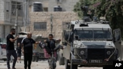 2024 年 8 月 28 日，以色列军队进入约旦河西岸城市杰宁展开军事行动。图为一名年轻人骑自行车经过一辆以色列装甲车。