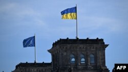 ທຸງຊາດຢູເຄຣນ (ເທິງ), ແລະທຸງຂອງຢູໂຣບ (ຊ້າຍ) ແນມເຫັນຢູ່ຕຶກອາຄານ Bundestag (ສະພາຕໍ່າຂອງເຢຍຣະມັນ) ໃນວັນທີ 24 ກຸມພາ 2025 ໃນນະຄອນຫຼວງ ເບີລີນ. 