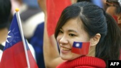 一名台灣女子臉頰上貼著台灣旗幟並手舉台灣旗幟參加集會。