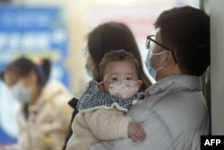 ເດັກທາລົກໃສ່ໜ້າກາກອະນາໄມ ຄອຍຖ້າກັບຄອບຄົວທີ່ພະແນກເດັກນ້ອຍທີ່ໂຮງໝໍໃນເມືອງຫາງໂຈວ ເຂດມົນທົນ ເຈີຈຽງຂອງຈີນ, ວັນທີ 6 ມັງກອນ 2025 (AFP)