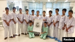泰國野豬足球隊員和教練豬著救援過程中喪生的前海軍海豹突擊隊員的畫像在青萊的醫院合影。